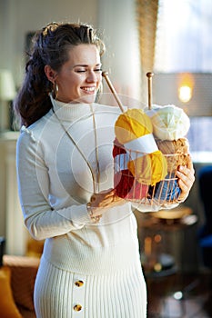 Smiling stylish woman holding basket with yarn and needles