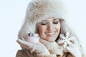 smiling stylish woman in winter coat and fur hat on white