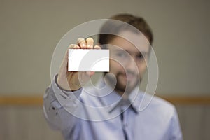 Smiling successful businessman holding white business card on concrete