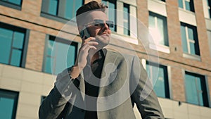 Smiling successful caucasian businessman man in sunglasses talking on mobile phone outdoors near office building in