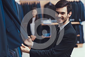 Smiling successful young man checks quality of jacket fabric in mens clothing store.
