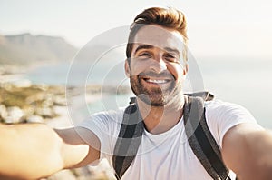 Smiling at the summit. Cropped portrait of a handsome young man taking selfies while hiking in the mountains.