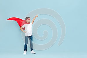 Smiling superhero boy in red mask and cape pointing hand aside