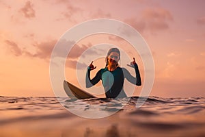 Smiling surfer woman sit on a surfboard in ocean.