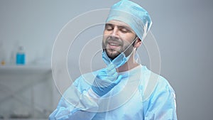 Smiling surgeon taking off medical face mask after successful operation, work