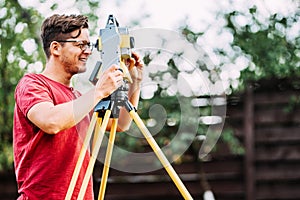 Smiling surveyor working with total station in garden