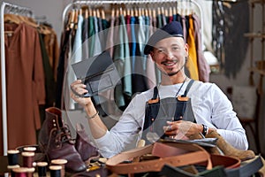 smiling talented craftsman holding leather handsmade thing in hands