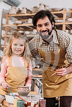 smiling teacher and happy child painting ceramic pot on pottery