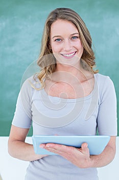 Smiling teacher holding tablet pc in front of blackboard