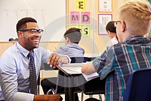 Smiling teacher kneeling beside elementary school pupilï¿½s desk