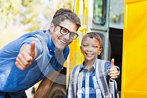 Smiling teacher and schoolboy showing thumbs up in front of school bus