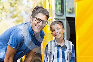 Smiling teacher and schoolboy standing in front of school bus