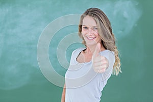 Smiling teacher standing thumbs up in front of blackboard