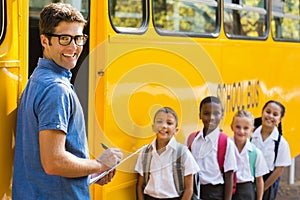 Smiling teacher updating check list of kids while entering in bus photo