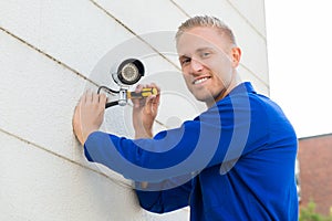 Smiling Technician Installing Camera On Wall