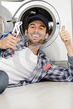 Smiling technician repairing washing machine while gesturing thumbs up