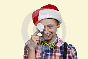 Smiling teen boy is closing his eye with santa hat's pompon.