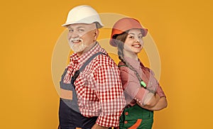 smiling teen child and grandfather builder in helmet on yellow background