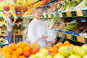 Smiling teen girl choosing fresh romaine lettuce in fruit and vegetable store