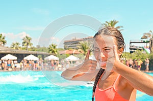 Smiling teen girl enjoing summer vacation at the hotel pool with palms and sun umbrellas on the background