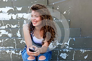 Smiling teen girl holding phone and sitting on steps