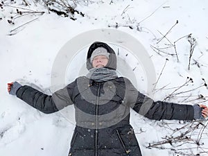 Smiling teen girl lies on the snow with her arms outstretched portrait