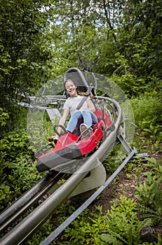 Smiling teen girl riding downhill on an outdoor roller coaster on a warm summer day.