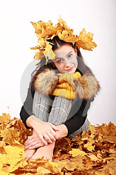 Smiling teen girl sitting on dried leaves with leaves in hair