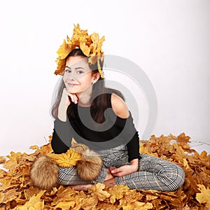 Smiling teen girl sitting on dried leaves with leaves in hair