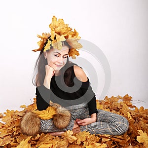 Smiling teen girl sitting on dried leaves with leaves in hair