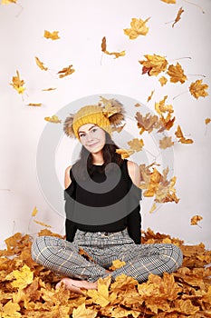 Smiling teen girl sitting under falling dried leaves