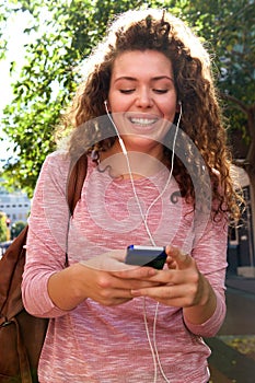 Smiling teen girl standing outside with mobile and earphones