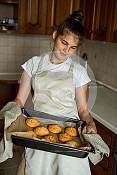 Smiling teen girl taking cookies out of the oven in the kitchen.Homemade cakes, cookies and gingerbread cookies. sweet breakfast