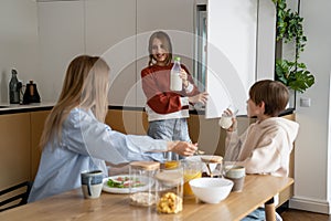 Smiling teen girl taking milk out of fridge while having breakfast with family at home