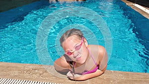 Smiling teen girl in water glasses in the swimming pool. Girl sitting on the border of the pool and making faces. Hot