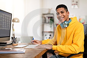 Smiling teen guy with headphones studying at desk