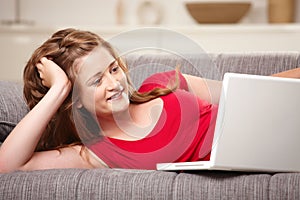 Smiling teen with laptop on sofa at home