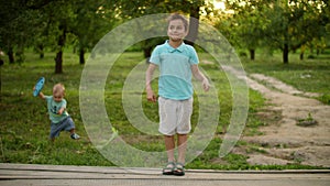 Smiling teenage boy dancing outdoors. Smaller kid carrying frisbee plate outside