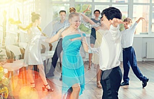 Smiling teenage boy and girl dancing waltz during Christmas event in college