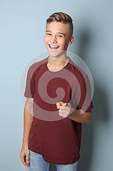 Smiling teenage boy pointing at viewer on color background