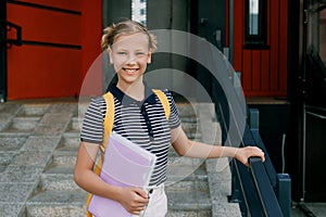 A smiling teenage girl with a backpack and a folder in her hands goes down the stairs, hurries to school. Back to school