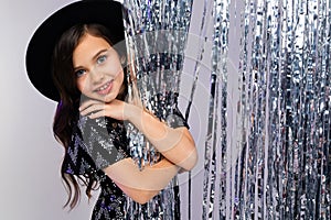 Smiling teenage girl in a black hat and elegant dress on a background of brilliant rain