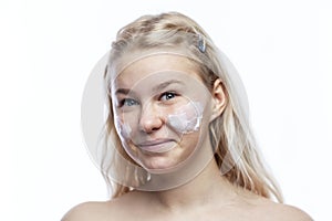 Smiling teenage girl with cream on her face. Cute blonde with freckles. Taking care of yourself from a young age. White background