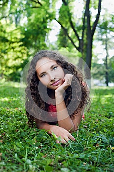 Smiling teenage girl with curly hair lying on a green grass
