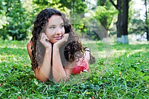 Smiling teenage girl with curly hair lying on a green grass