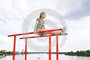 Smiling teenage girl doing gymnastic exercises on uneven bars in city conditions outdoors
