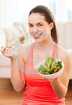 Smiling teenage girl with green salad at home