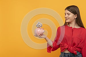 Smiling teenage girl holds piggy bank with dollars. Concepts of saving money and investments. Financial planning, savings