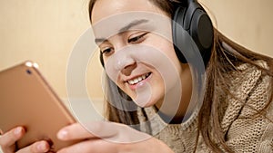 Smiling teenage girl listening music in headphones and using tablet computer on bed