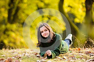 Smiling teenage girl lying on autumn maple leaves at fall outdoors. Portrait of a beautiful smiling teenager. Young teen